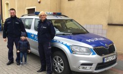 Na zdjęciu widać 5-letniego Maksa w towarzystwie dwóch funkcjonariuszy Policji, wszyscy stoją przy radiowozie
