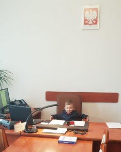 Na zdjęciu widać 5-letniego Maksa, który siedzi na fotelu za biurkiem w gabinecie Komendanta Powiatowego Policji w Ostrzeszowie