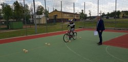 Na zdjęciu widać chłopca jadącego na rowerze, który pokonuje przeszkodę tak zwaną żmijkę, jest to przejazd po między okrągłymi przeszkodami ustawionymi w zygzak