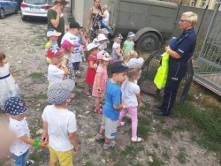 Na zdjęciu widać grupę dzieci w wieku przedszkolnym oraz funkcjonariuszkę Policji
