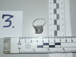 Obraz przedstawia biżuterię w postaci pierścionka, który położon jest na biurku przy dwóch miarkach