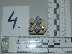 Obraz przedstawia biżuterię w postaci zawieszek i kolczyków, które położony jest na biurku przy dwóch miarkach