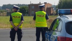 Na zdjęciu widać dwóch Policjantów stojących obok radiowozu, prowadzących obserwację drogi.